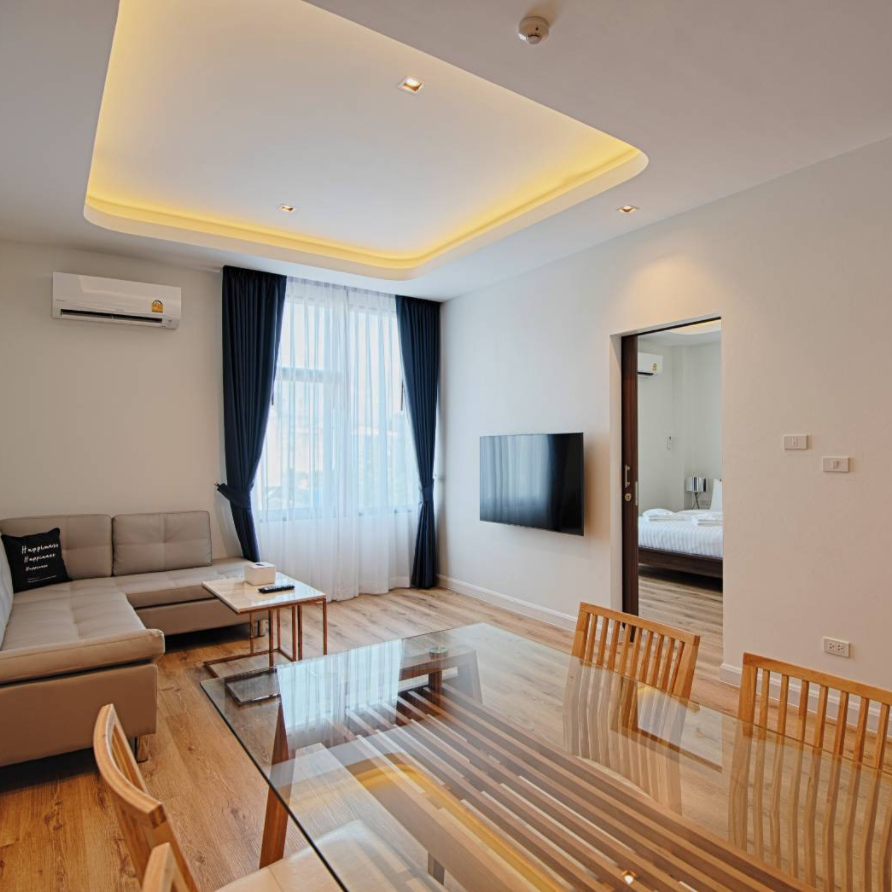 Living room with beige sectional sofa, glass dining table, TV, and open doorway to a bedroom.