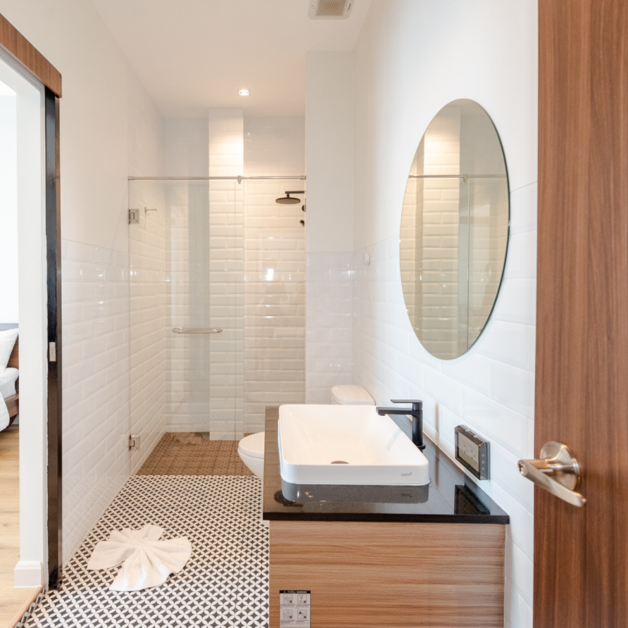 Modern bathroom with white subway tile shower, geometric floor tile, round mirror, and wooden vanity.