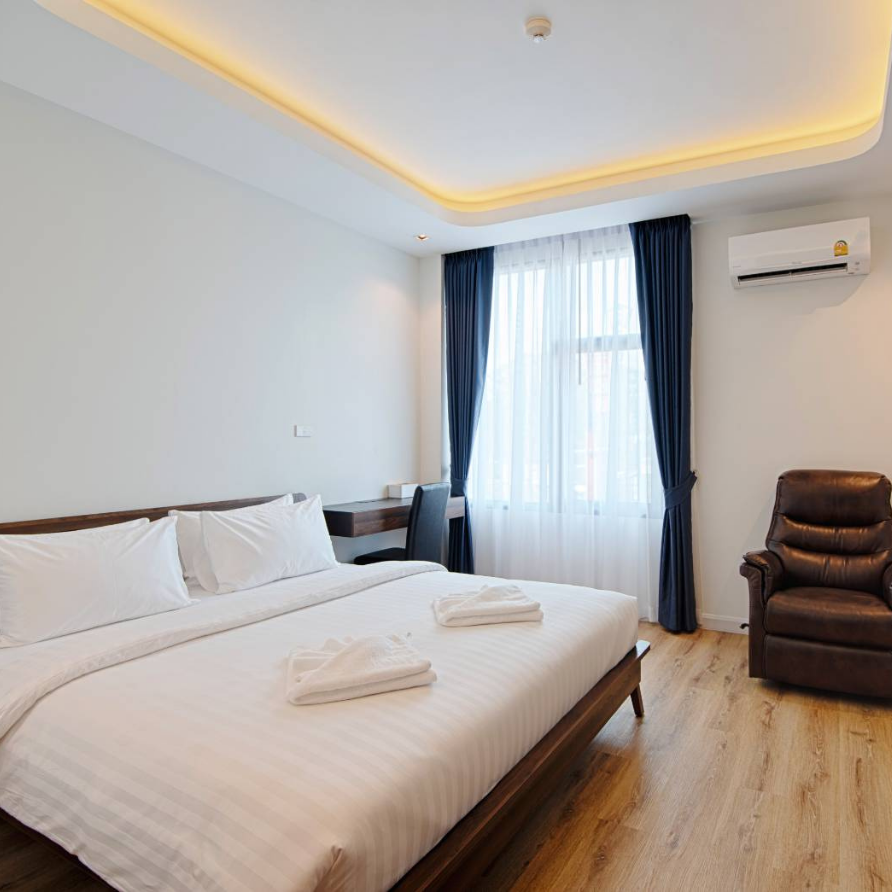 Bedroom with a large bed, desk, armchair, and window with blue curtains; neutral colors.