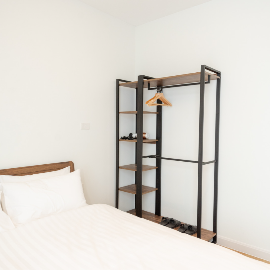 Bedroom with a bed and an open wardrobe with clothes hanger and shelves.