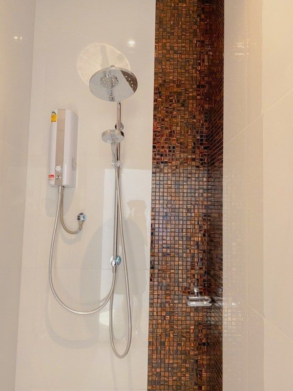 Shower with white and chrome fixtures against white and mosaic tile walls.