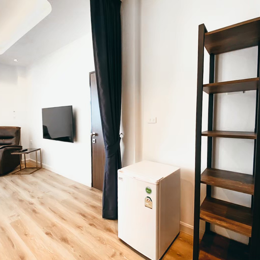Interior with TV, refrigerator, bookshelf, and a dark curtain in a room with light wood flooring.