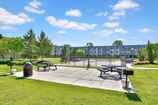 Outdoor picnic area with tables, grills, and apartment building in the background under a blue sky.