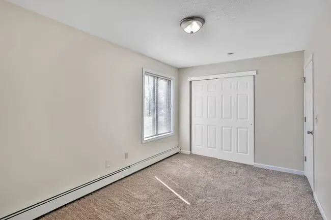 Empty bedroom with beige walls, brown carpet, white closet and door, small window.
