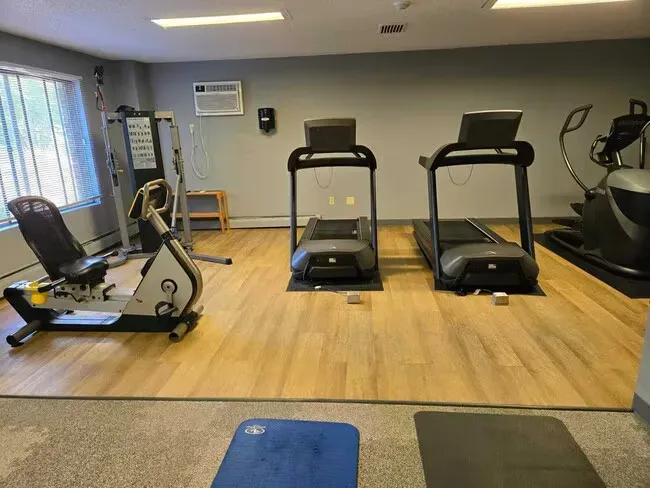Gym with treadmills, elliptical, recumbent bike, and weight machine, on a light wood-look floor.