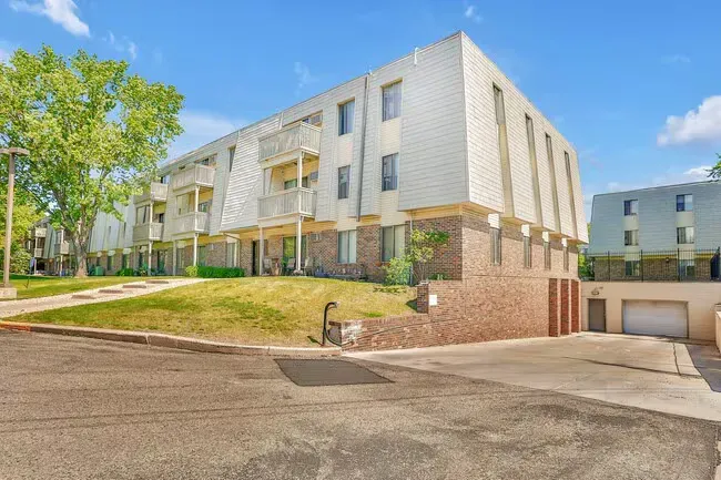 Multi-story apartment building with brick and white siding, drive-under garage, and green lawn.