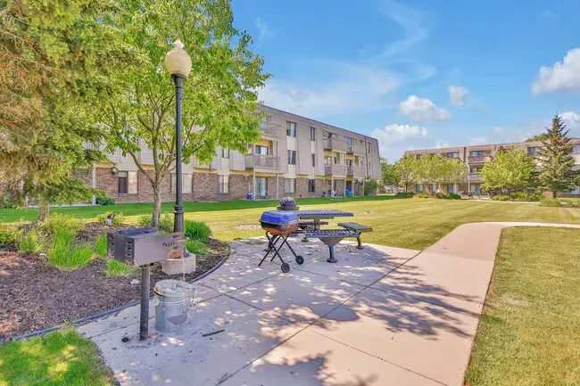 Park with grill, picnic table, and apartment buildings under blue sky.
