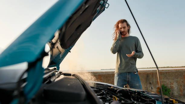 A man is standing next to a broken-down car talking on a cell phone.
