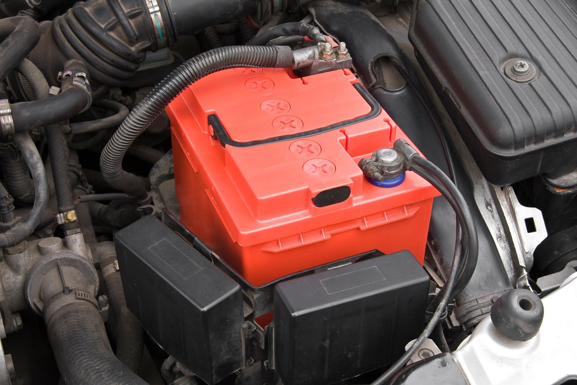 A red battery is sitting under the hood of a car.