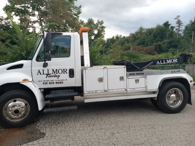 A white allmor tow truck is parked on the side of the road.
