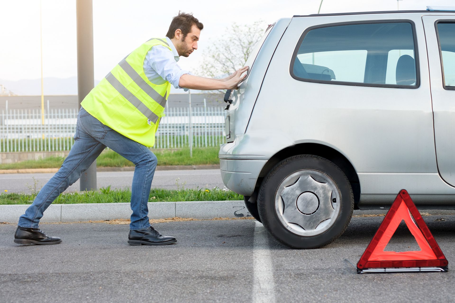 A man is pushing a broken down car in a parking lot.
