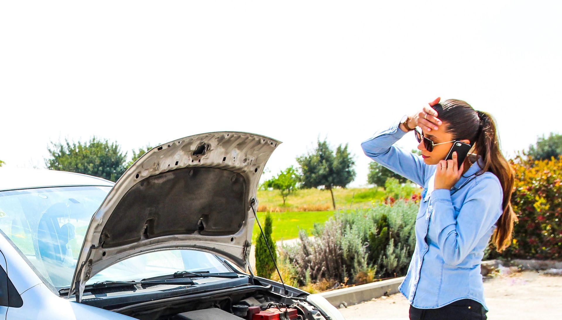 A woman is talking on a cell phone next to a broken down car.