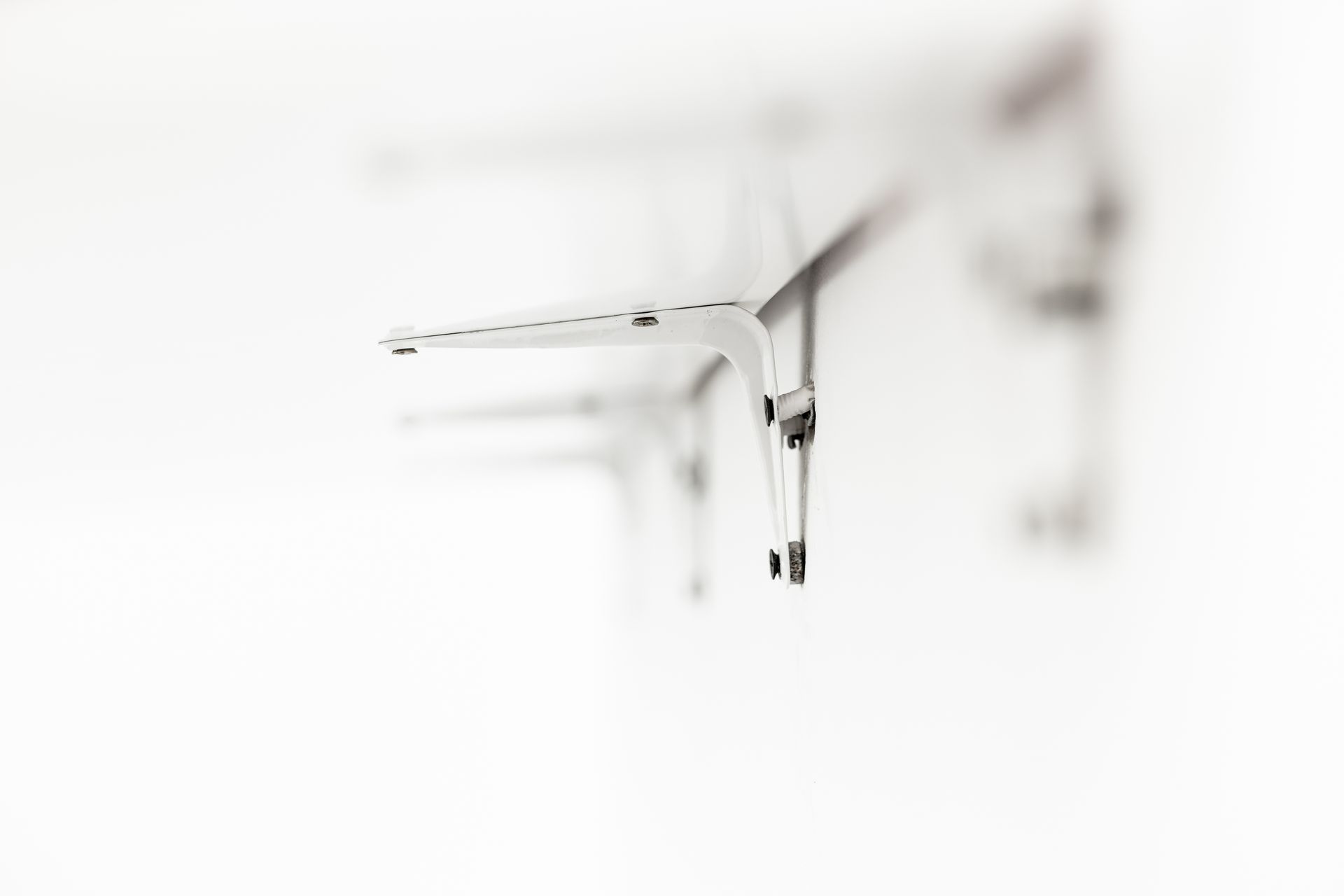 A close-up, shallow-focus shot of a white metal shelf bracket mounted on a bright, out-of-focus white wall.