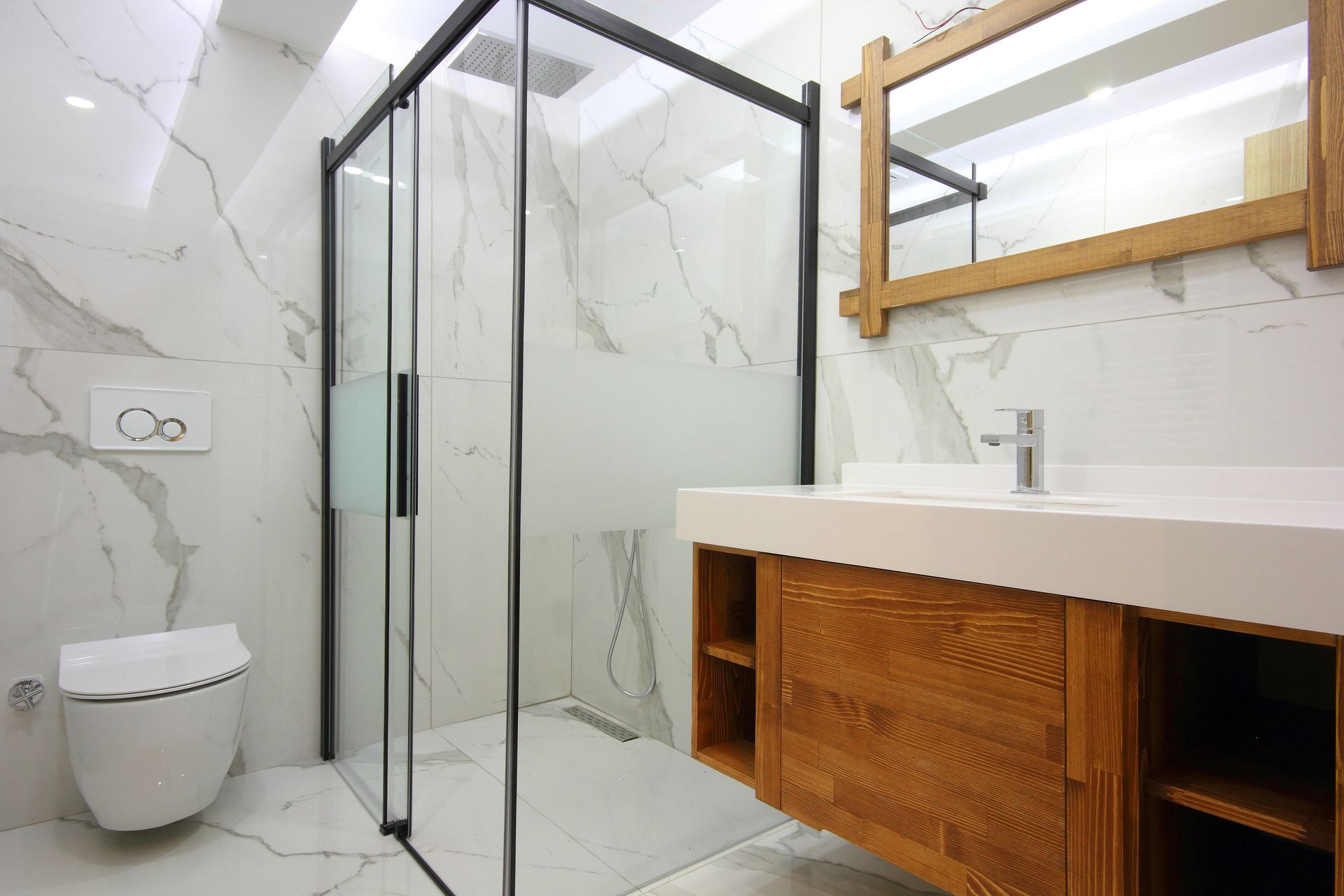 Modern bathroom with white marble-patterned walls, a glass shower stall, a wood vanity, and a wall-mounted toilet.