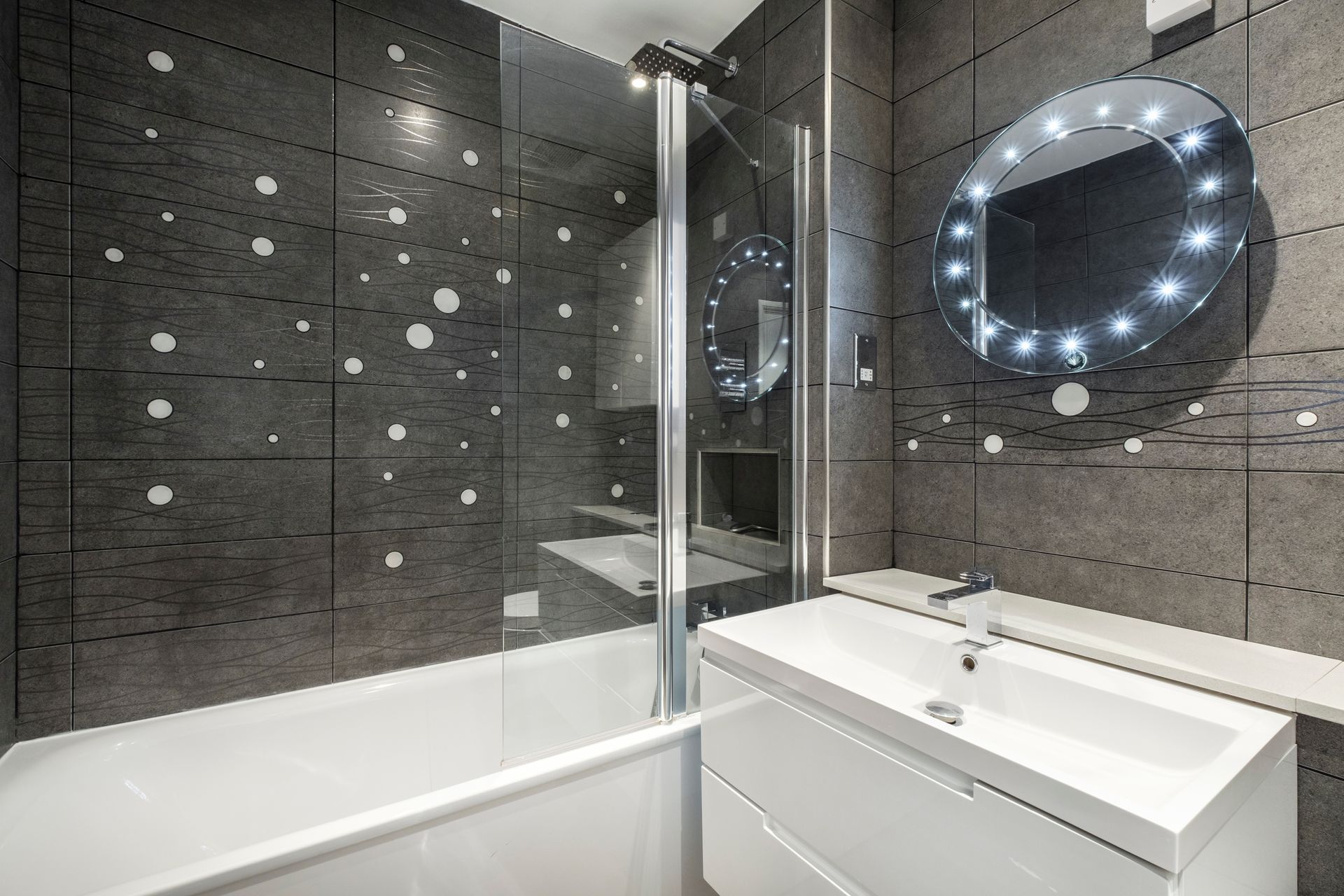 A modern bathroom featuring a white bathtub, a sleek vanity sink, and dark tiled walls decorated with small, white spots.