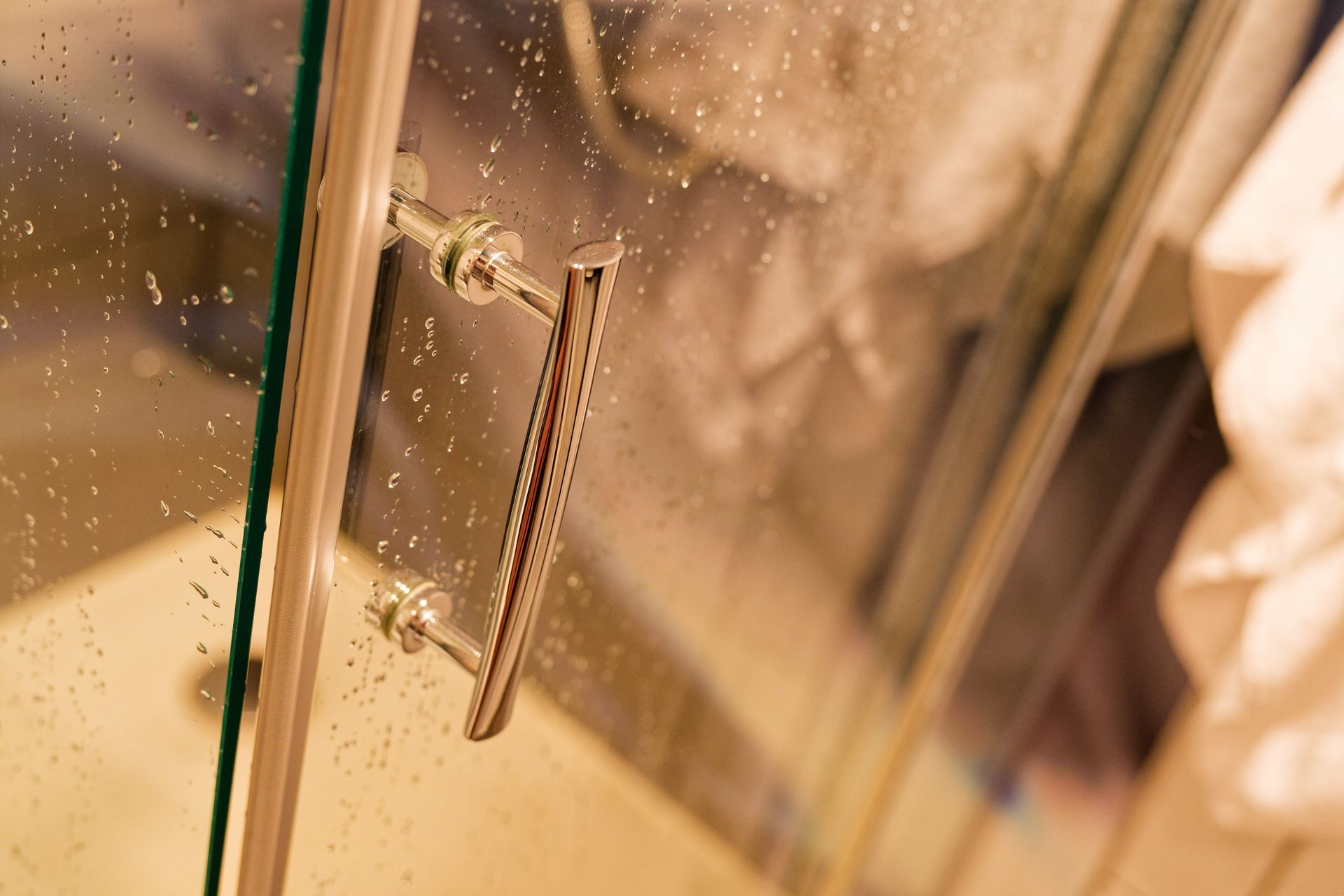 A close-up of a metal shower door handle attached to a glass door covered in water droplets.