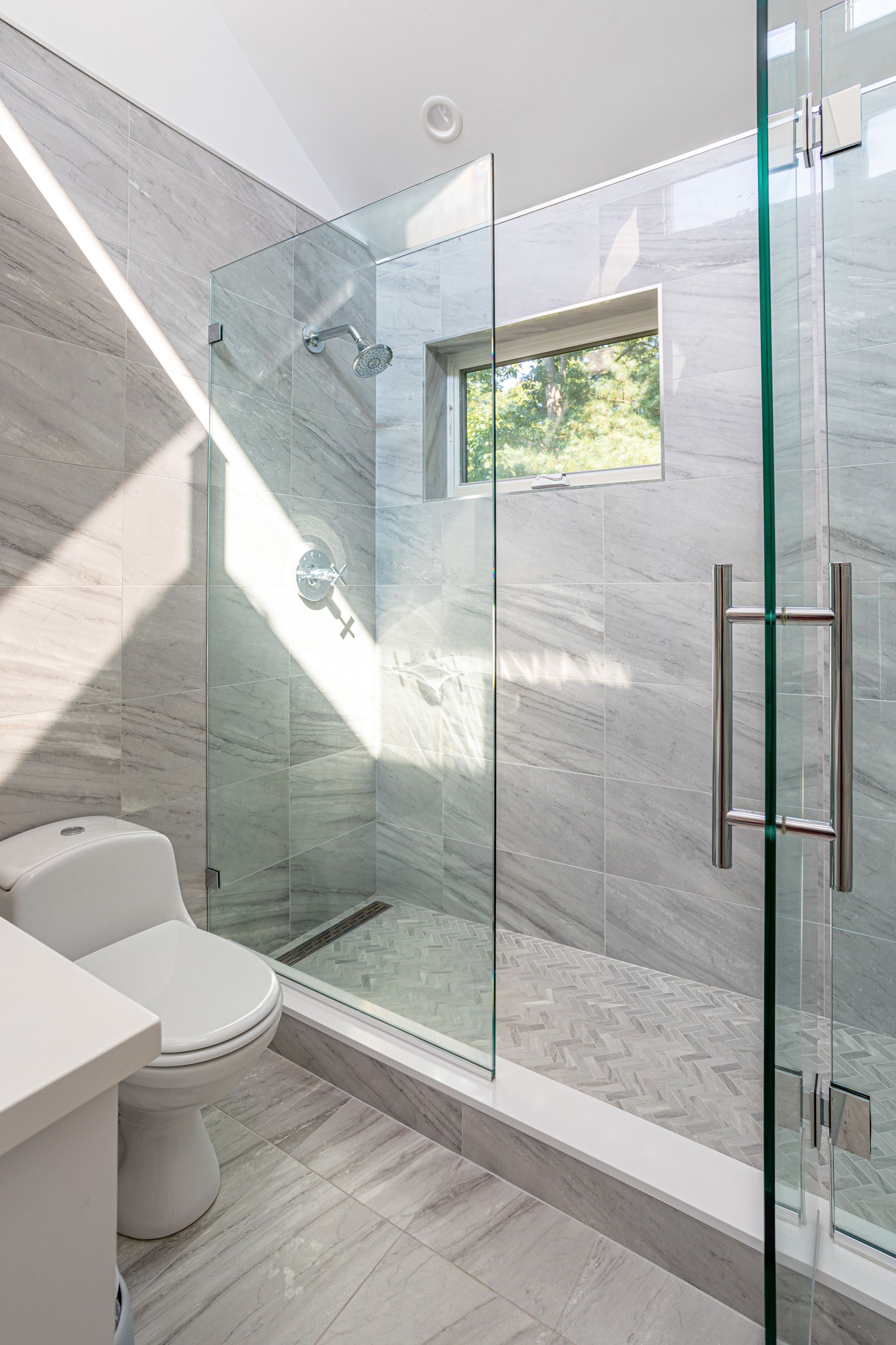 Modern bathroom featuring a glass-enclosed walk-in shower with gray stone tiles and a white toilet.