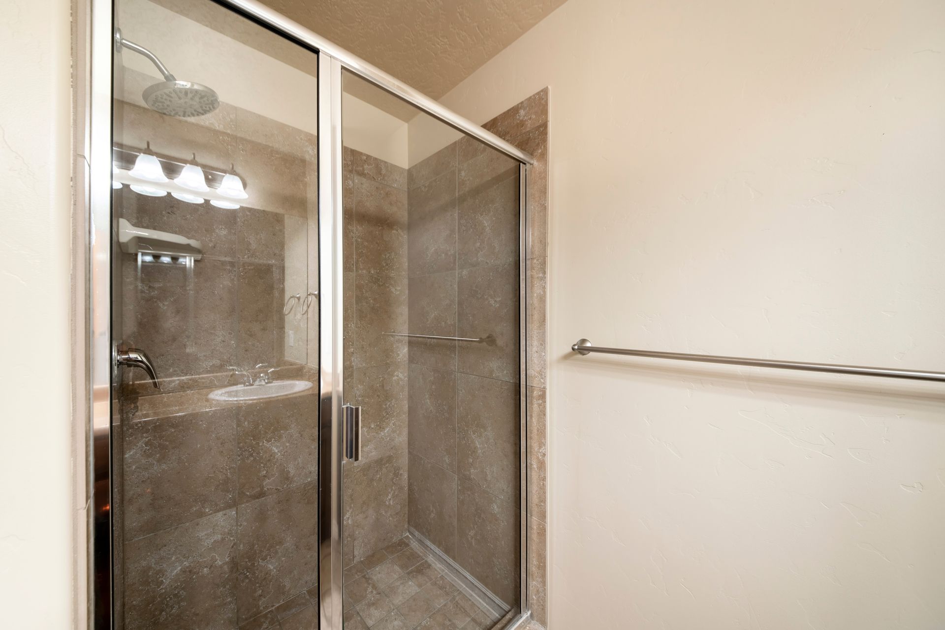 A glass shower enclosure with beige tiled walls in a bathroom next to a towel bar on a plain wall.