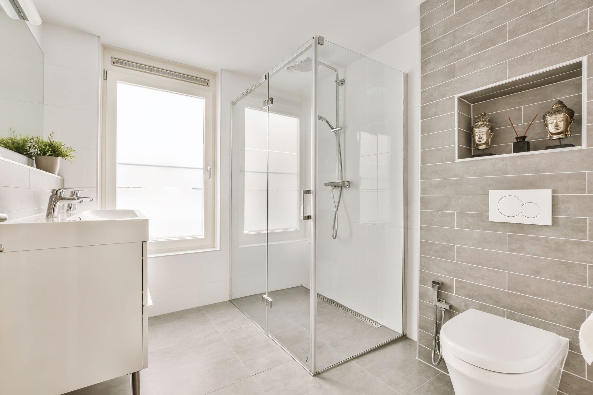Modern bathroom with a glass-enclosed shower, a white vanity, a wall-mounted toilet, and gray tiled walls with a wall niche.
