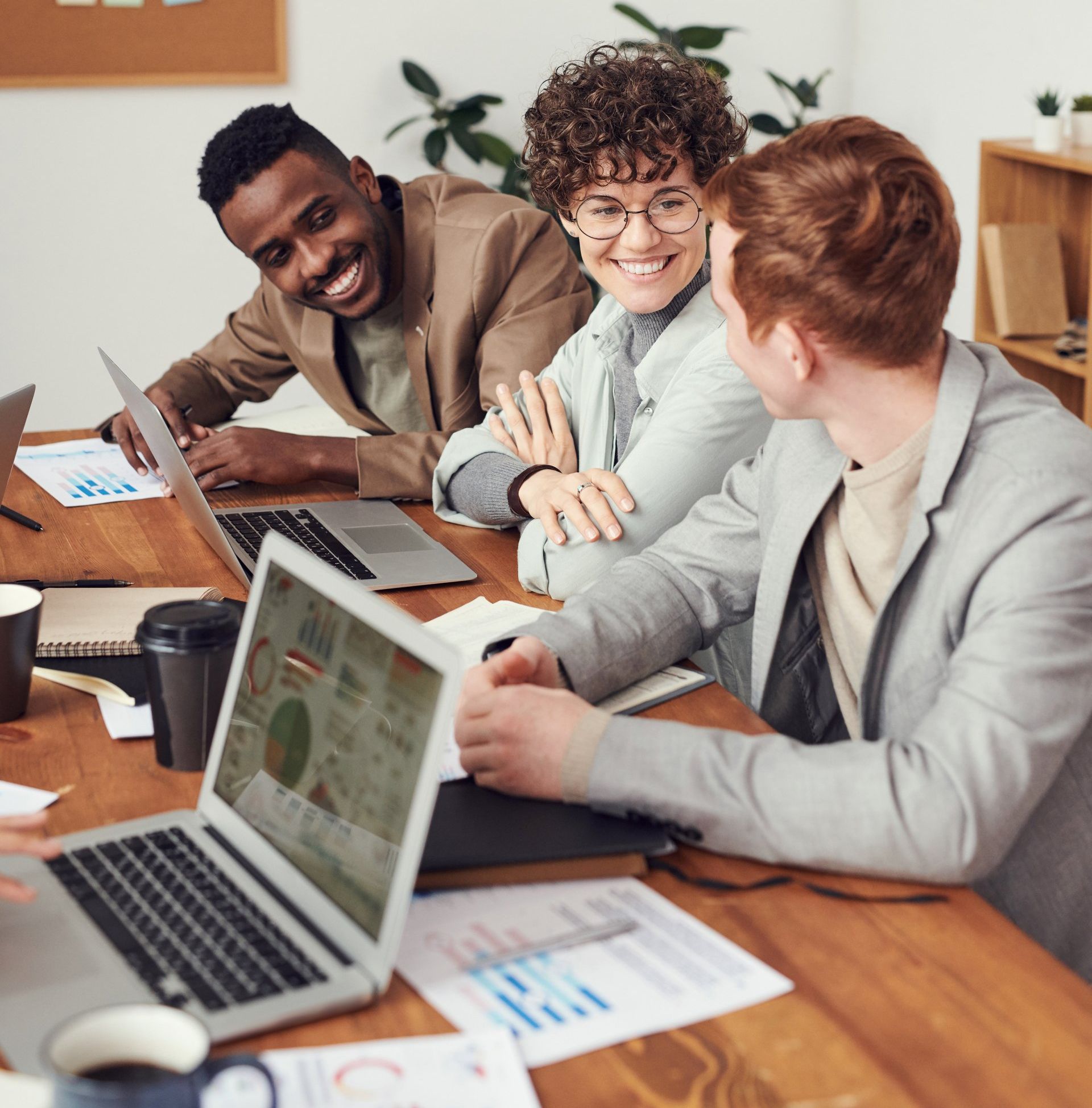 A group of people are sitting at a table with laptops and papers