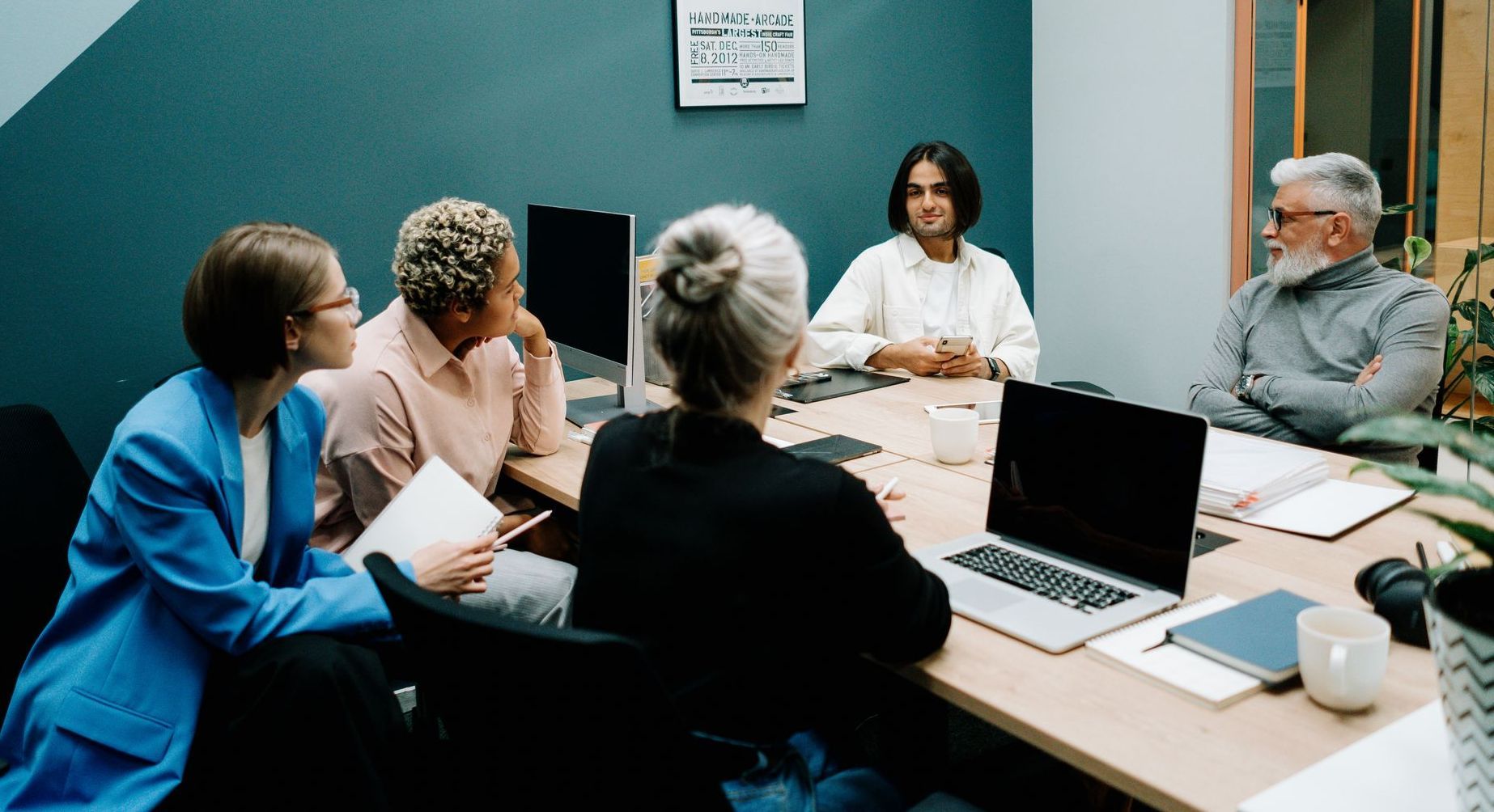 A group of people are sitting around a table with laptops.