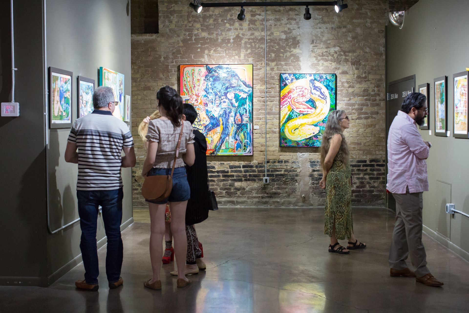a group of people are looking at paintings in a museum .