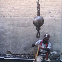 a man is sitting in front of a brick wall with a crane hook hanging from the ceiling .