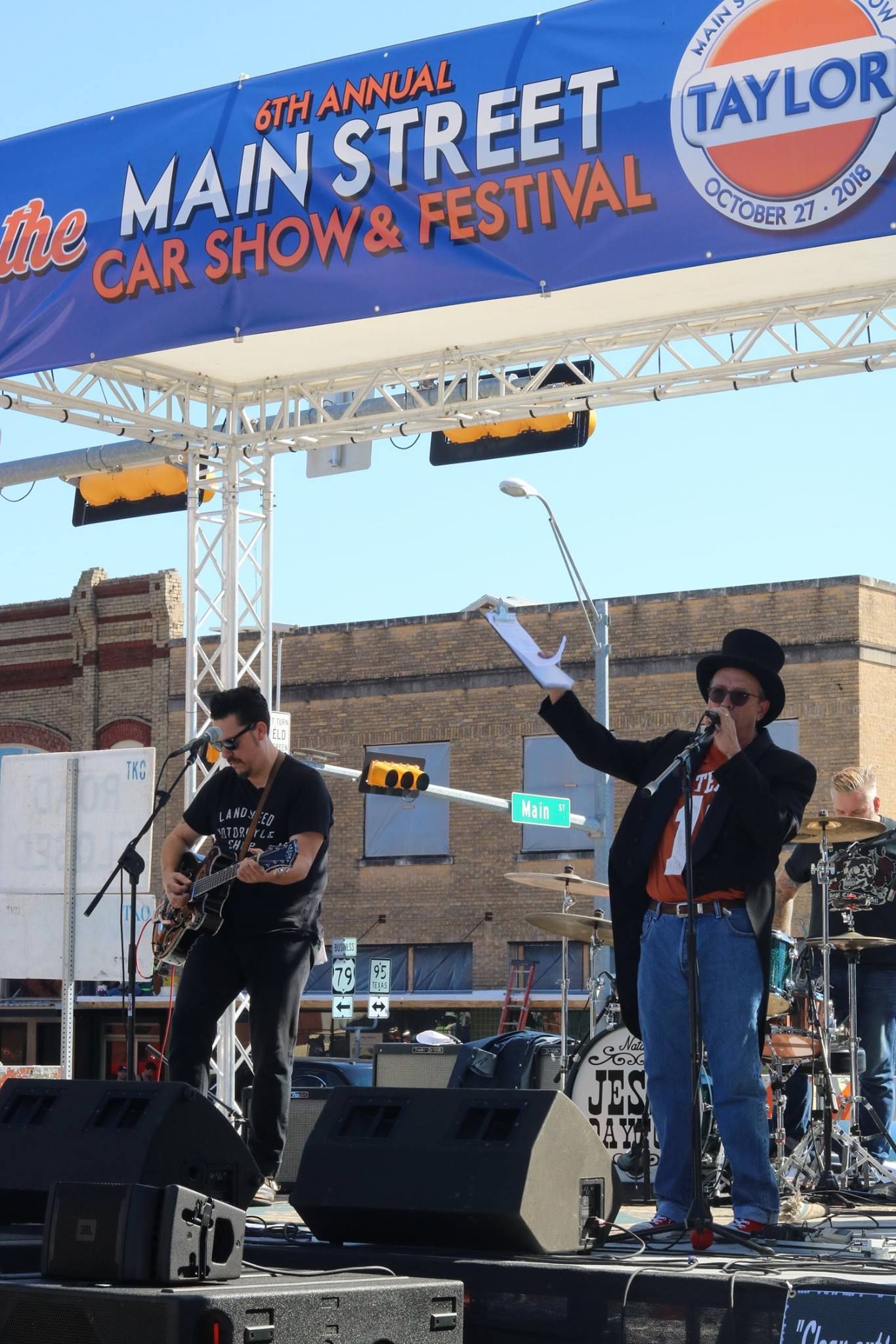 a man in a top hat is speaking into a microphone at the main street car show and festival