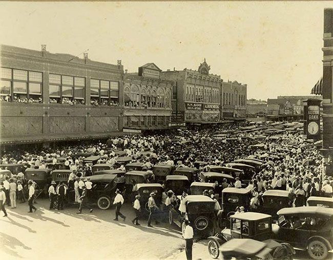 a black and white photo of a crowd of people and cars