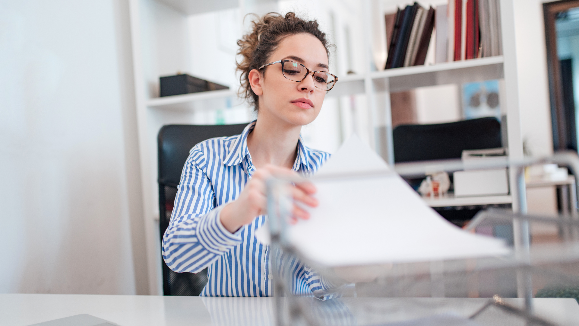 A woman is sitting at a desk in an office looking at a piece of paper.