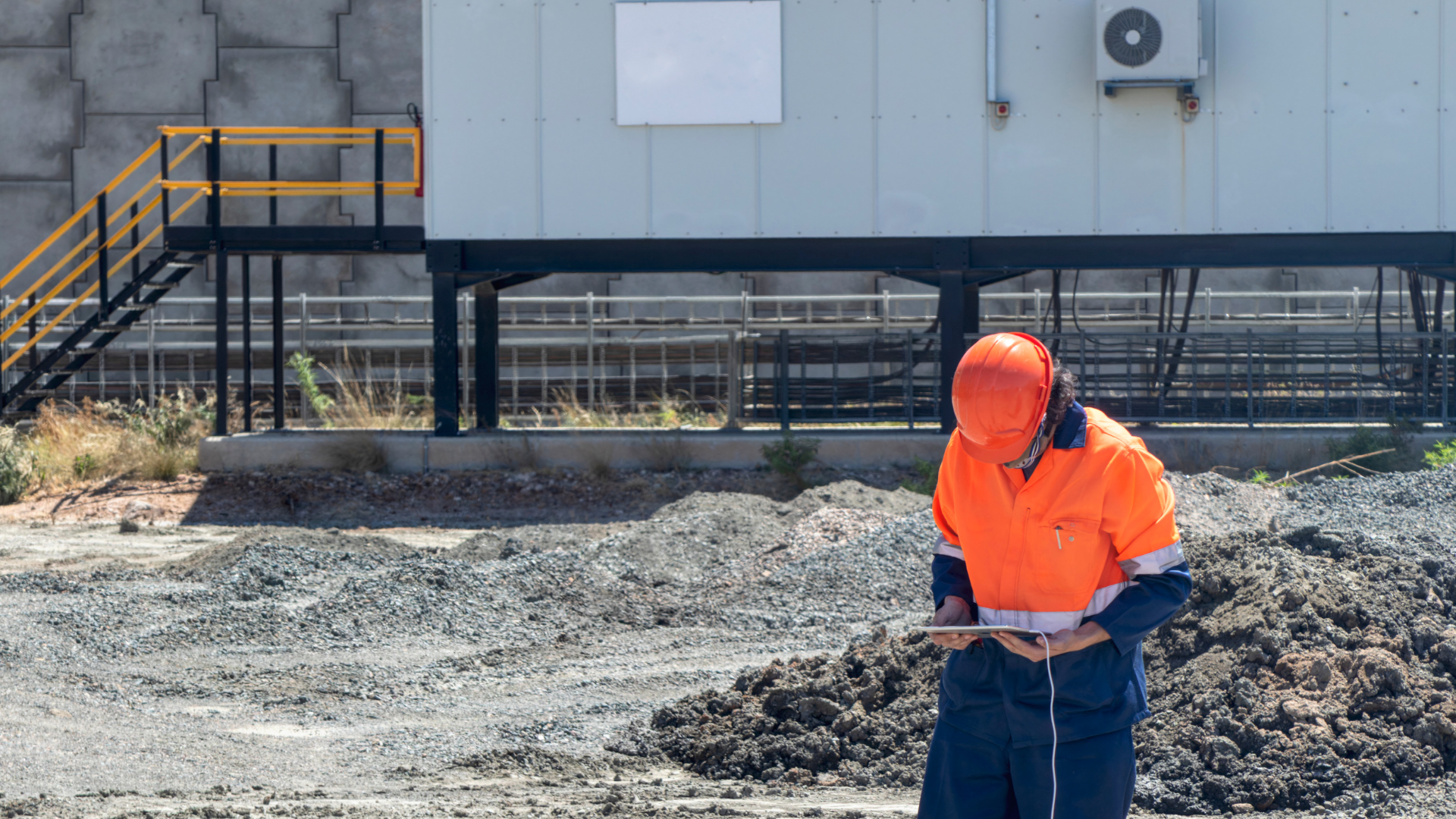A construction worker is standing in a pile of dirt in front of a building.