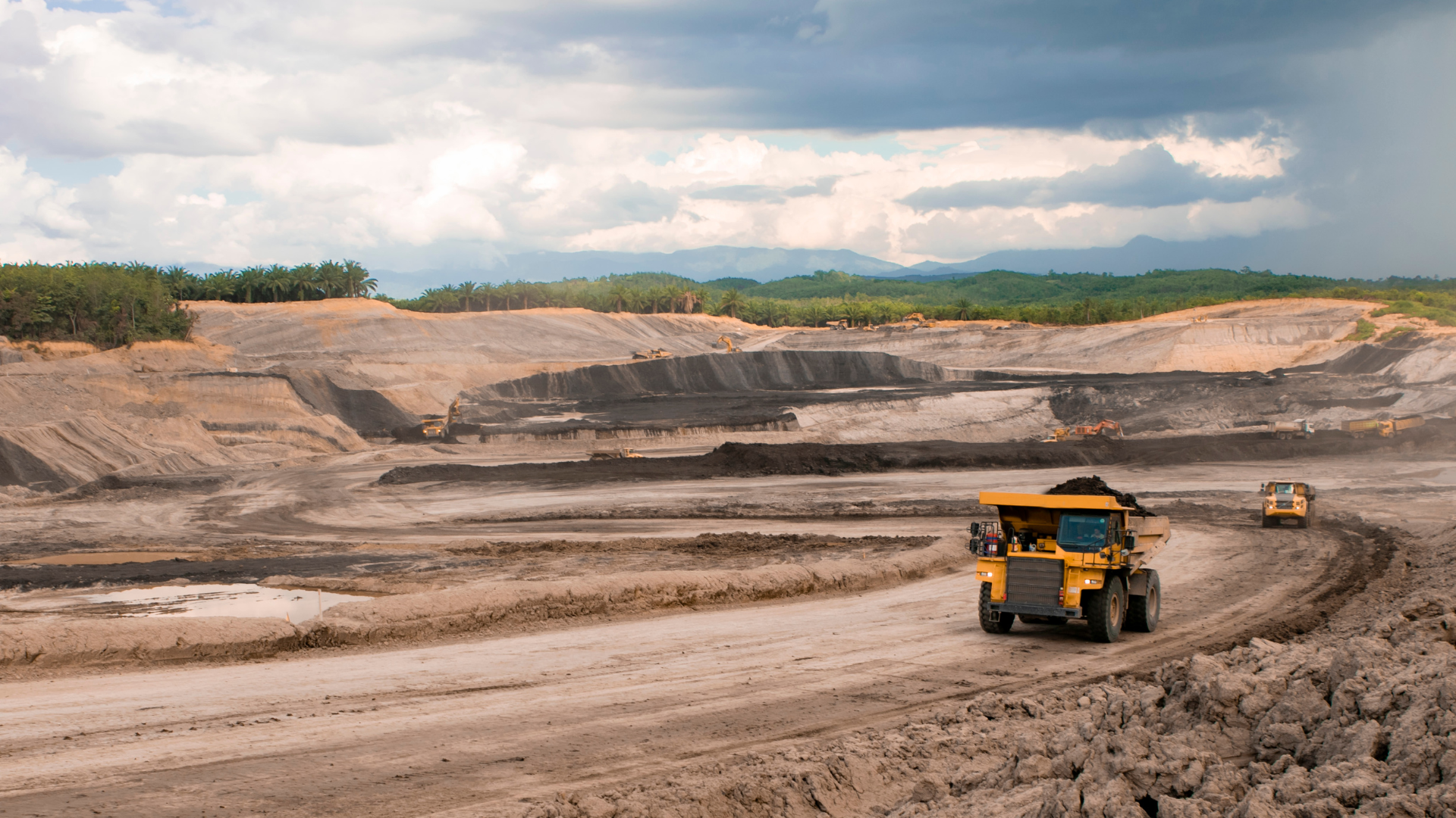 A yellow dump truck is driving down a dirt road in a mine.