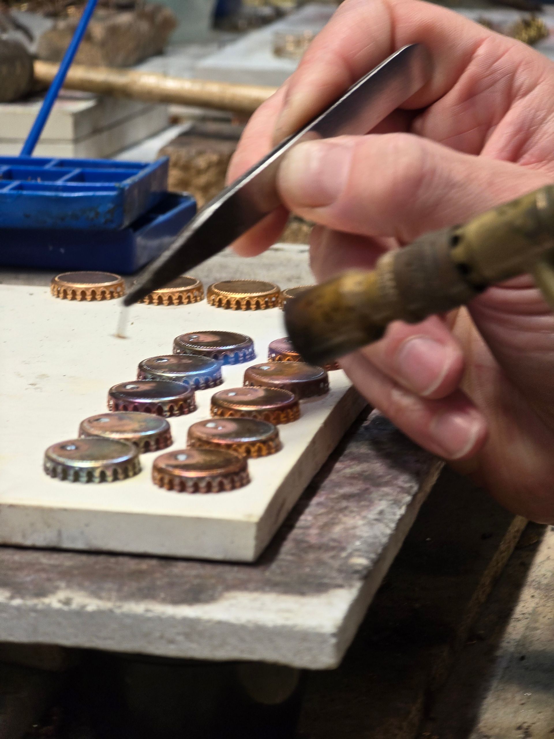 一名男子用焊槍焊接瓶蓋，用鑷子將焊錫放置在陶瓷表面上。