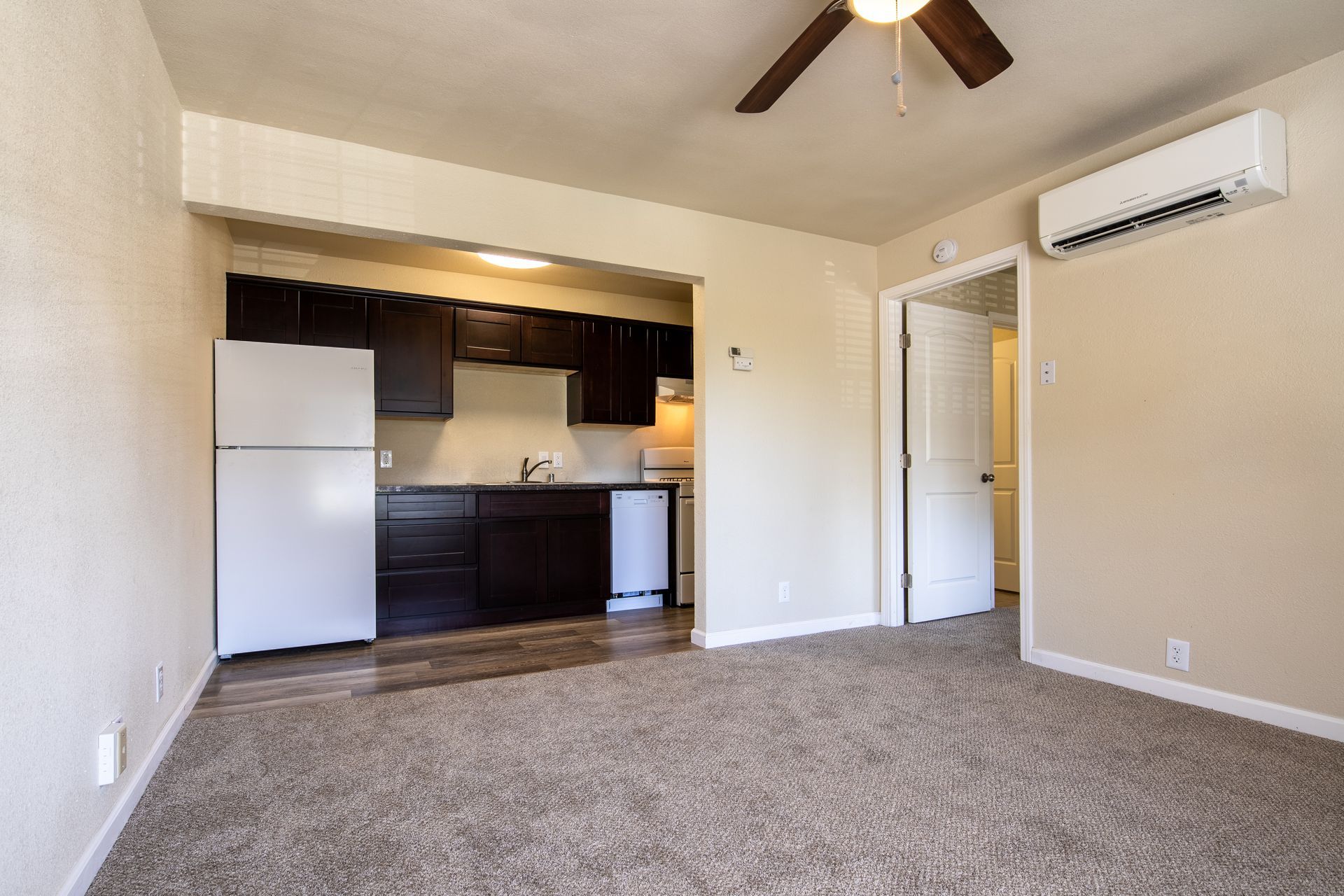 Small apartment interior with a kitchen, fridge, and open doorway.