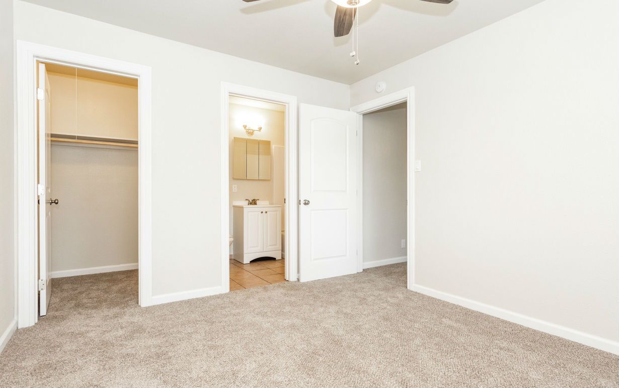 Empty bedroom with three white doors, tan carpet, and ceiling fan.