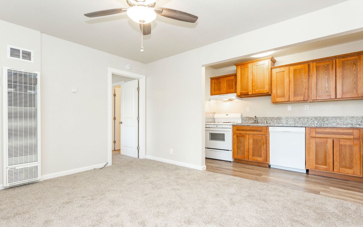 Cozy interior with tan carpet, a kitchen, and a white and wooden cabinet.