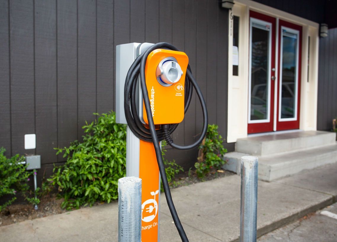 Orange EV charging station in front of a building with red doors.