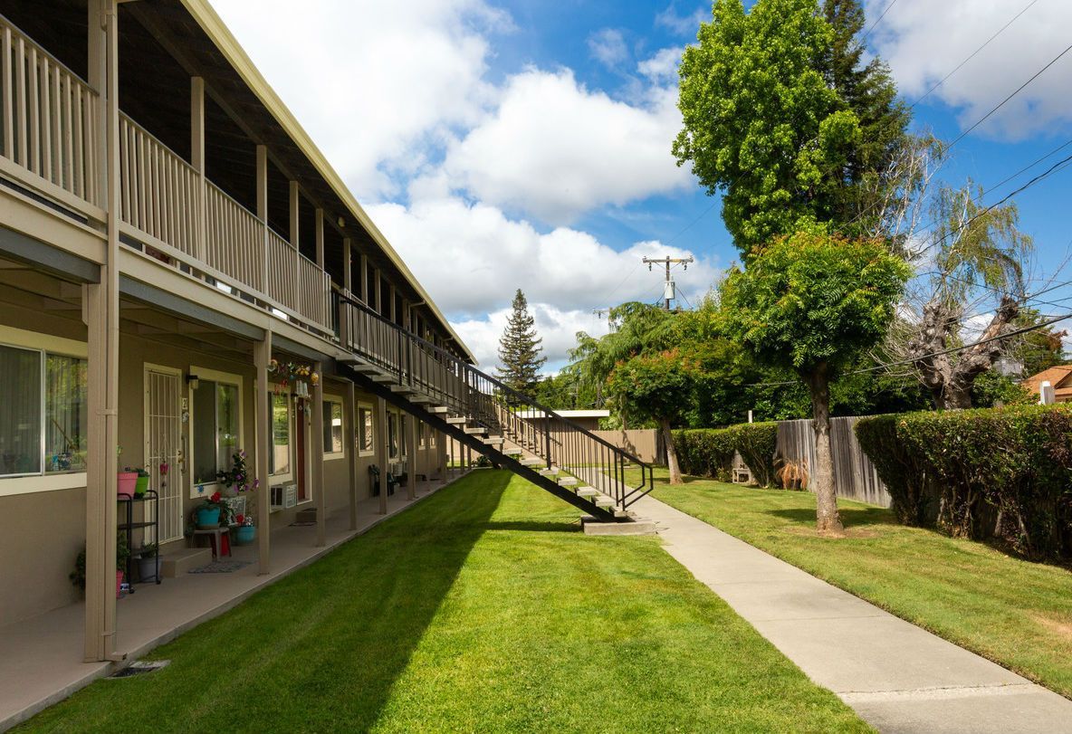 Apartment complex exterior with grass walkway, stairway, and blue sky.