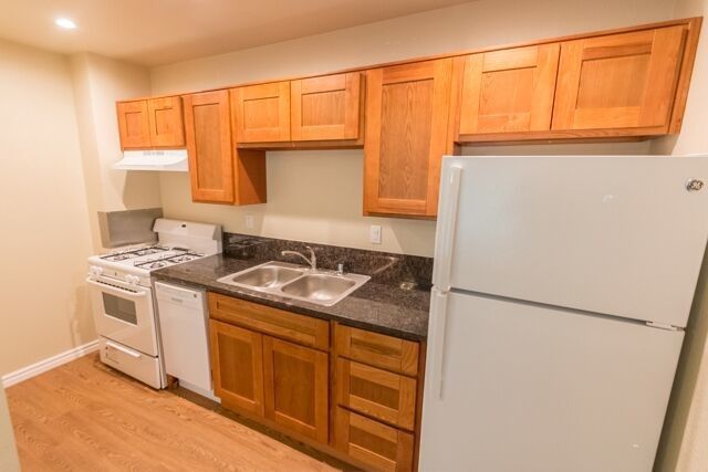 Small kitchen with wood cabinets, white appliances, and a granite countertop.