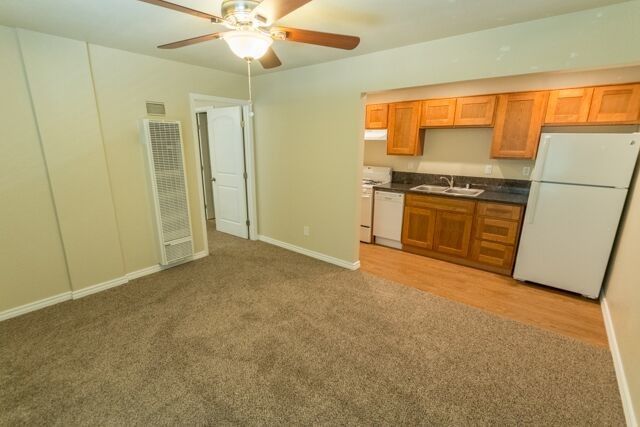 Empty apartment interior with carpet, kitchen cabinets, and a white refrigerator.