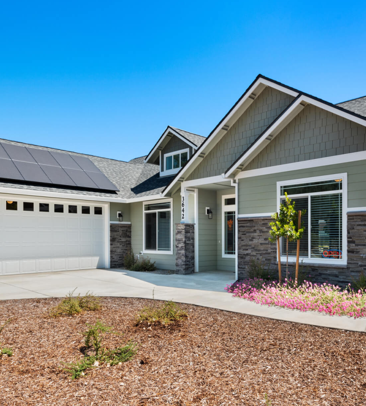 Green house with solar panels on the roof, white garage door, and stone accents.