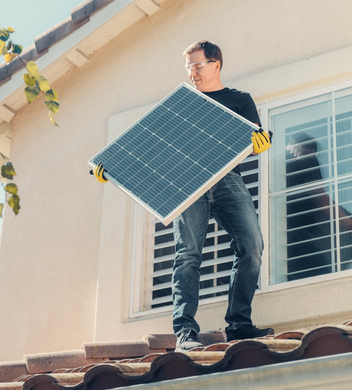 Man in gloves carries solar panel on a rooftop.