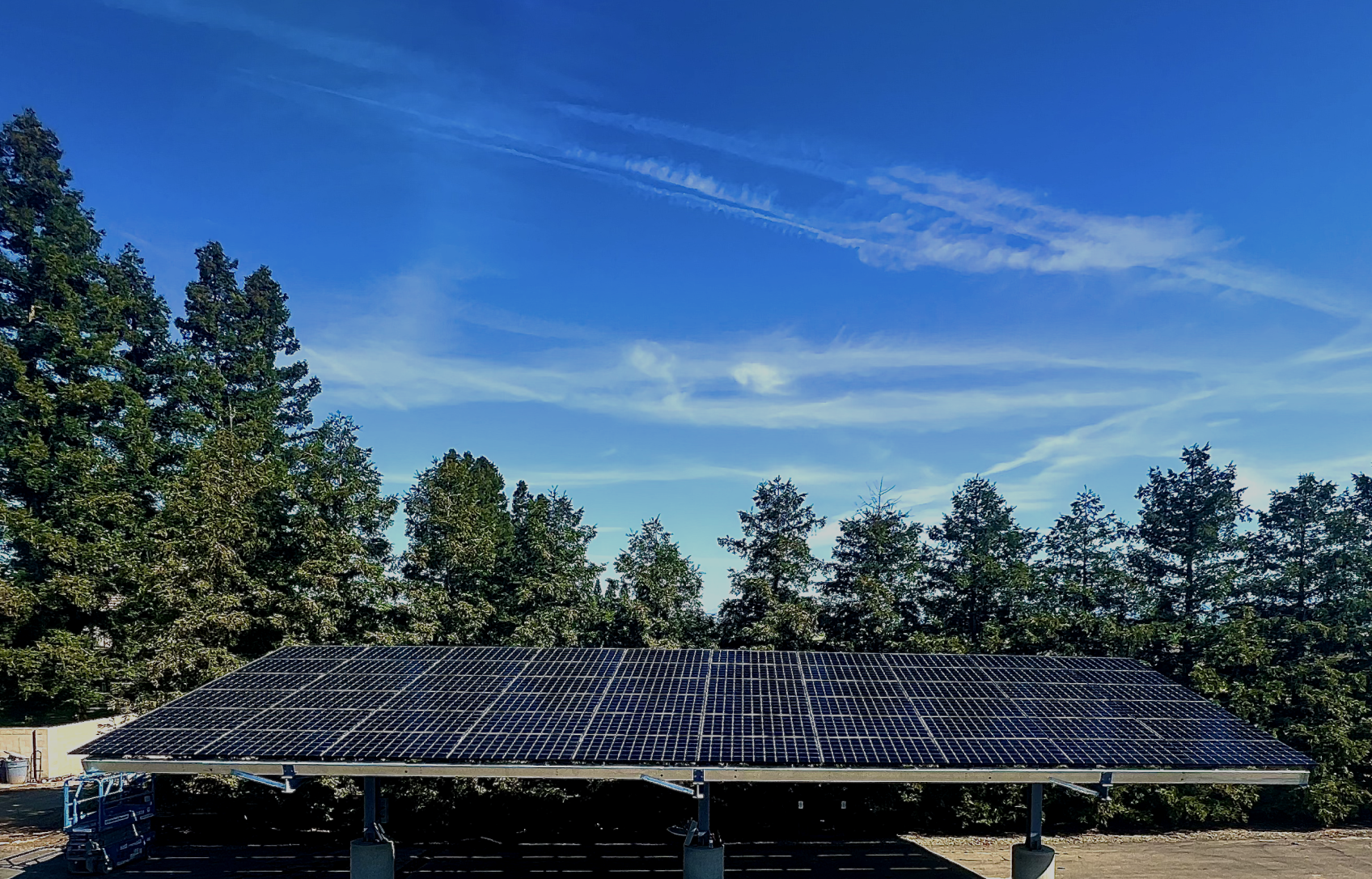 Solar panels over a parking structure with trees and a blue sky with clouds in the background.