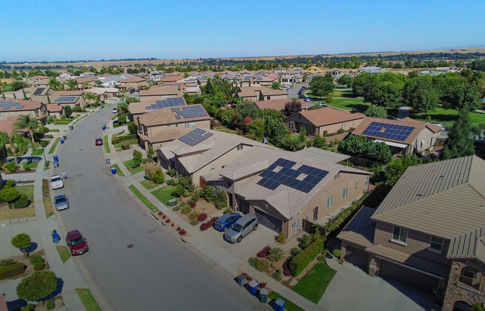 Aerial view of a suburban neighborhood with houses, solar panels, and a street on a sunny day.