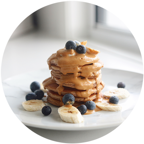 A stack of pancakes with peanut butter , bananas and blueberries on a plate.