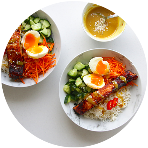 Two bowls of food with rice , eggs , carrots and cucumbers on a table.