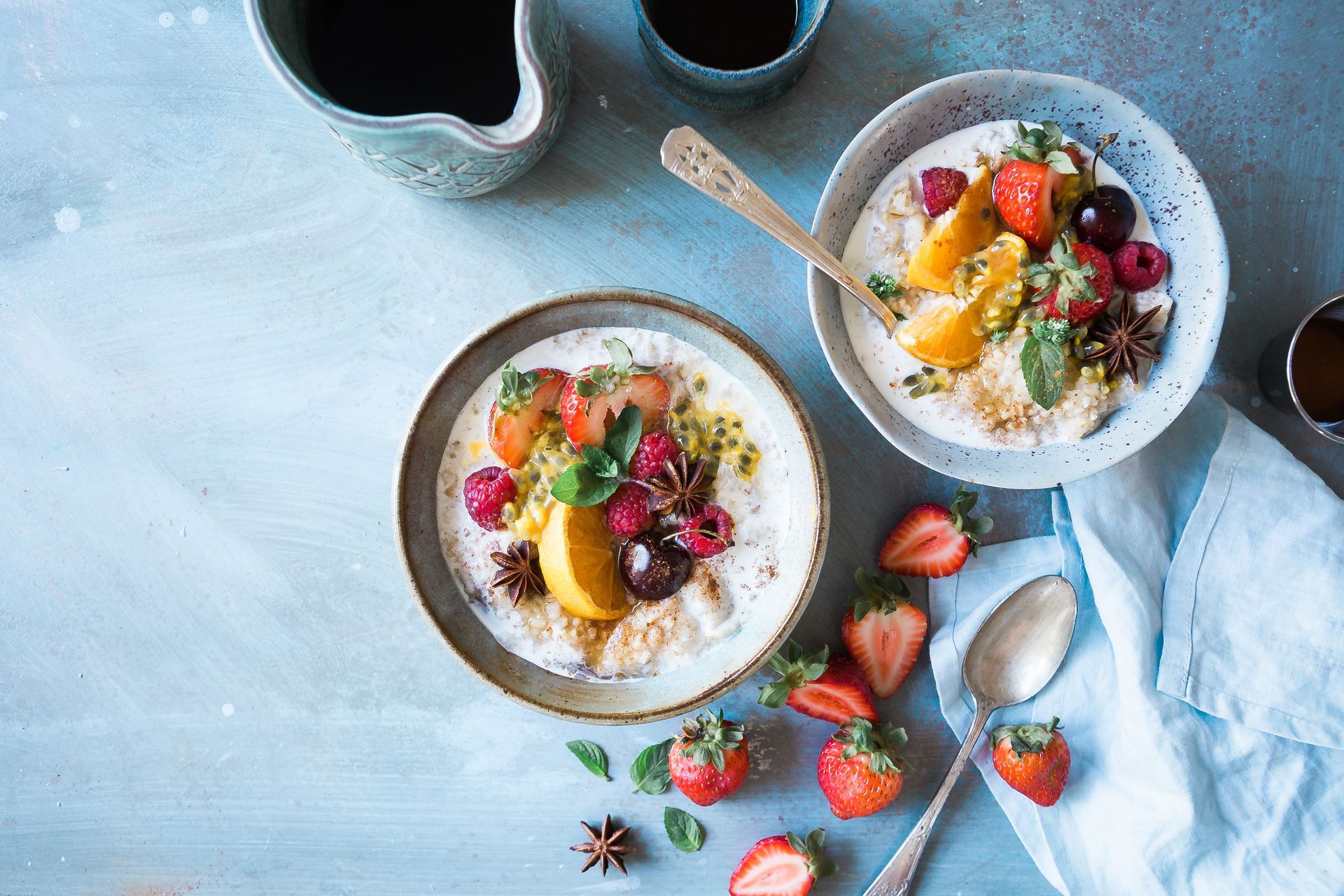Two bowls of oatmeal with fruit and a pitcher of coffee on a table.