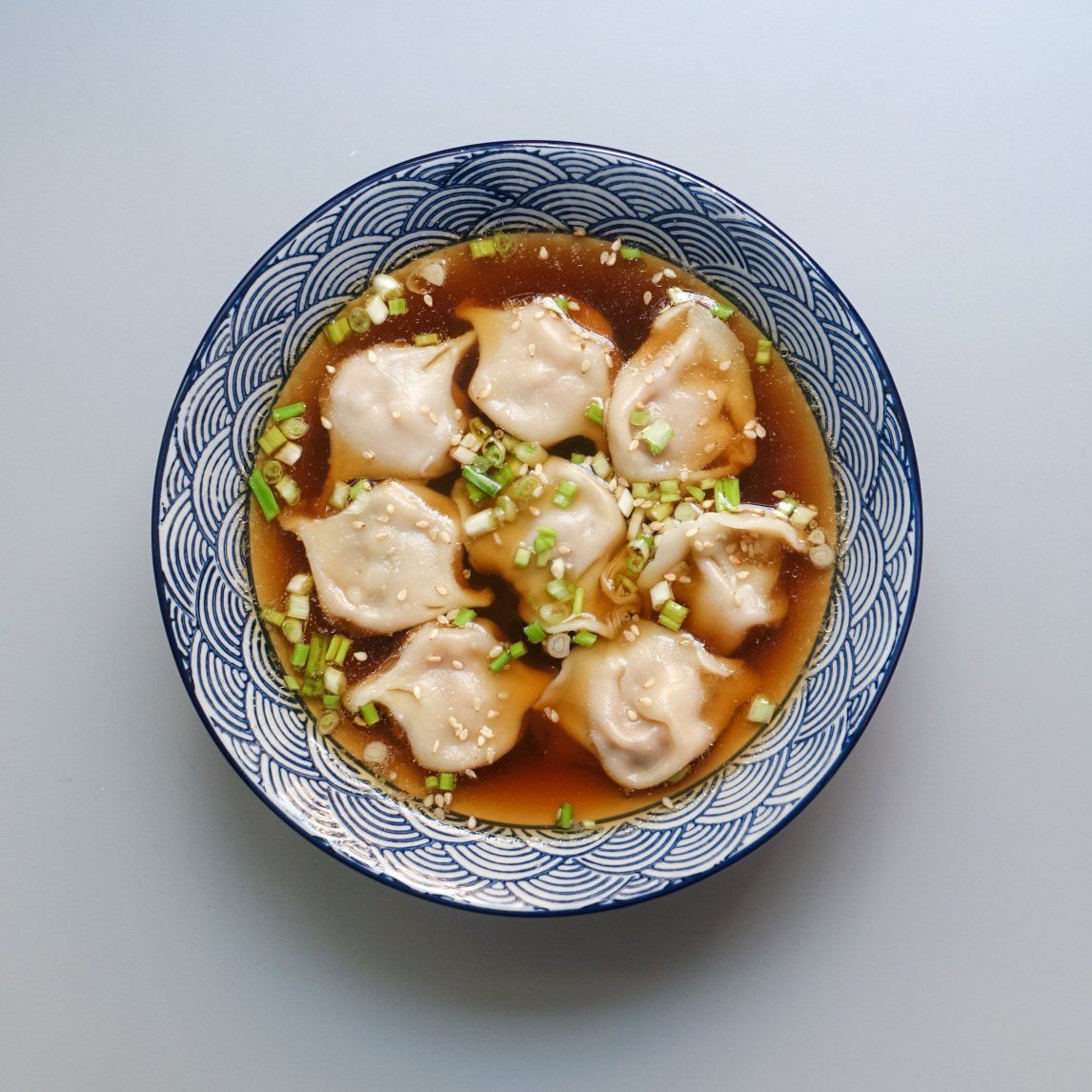 A bowl of wonton soup with green onions on top