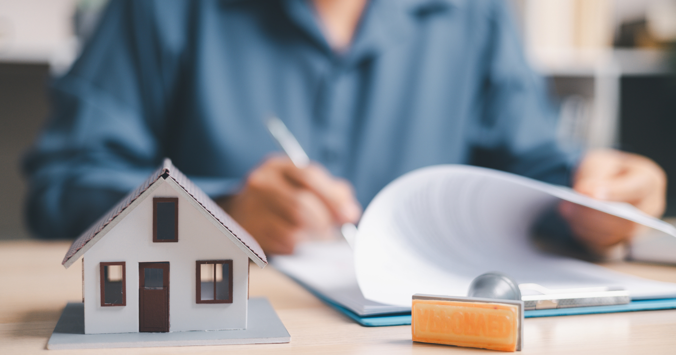 Miniature house model and key in front of a person writing paperwork at a desk