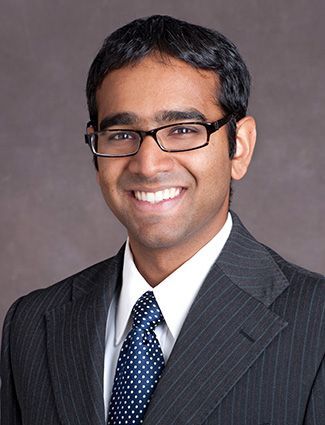 A smiling doctor in a lab coat with a stethoscope around his neck.